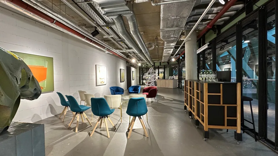 Long view through the gallery with chairs, paintings on the walls and the bar along the glass front